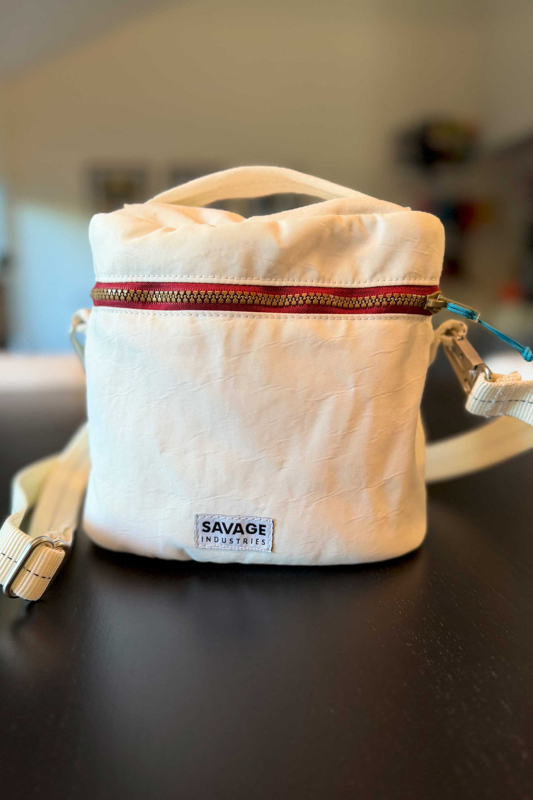 White bag with a red zipper and 'Savage Industries' logo on a dark surface.