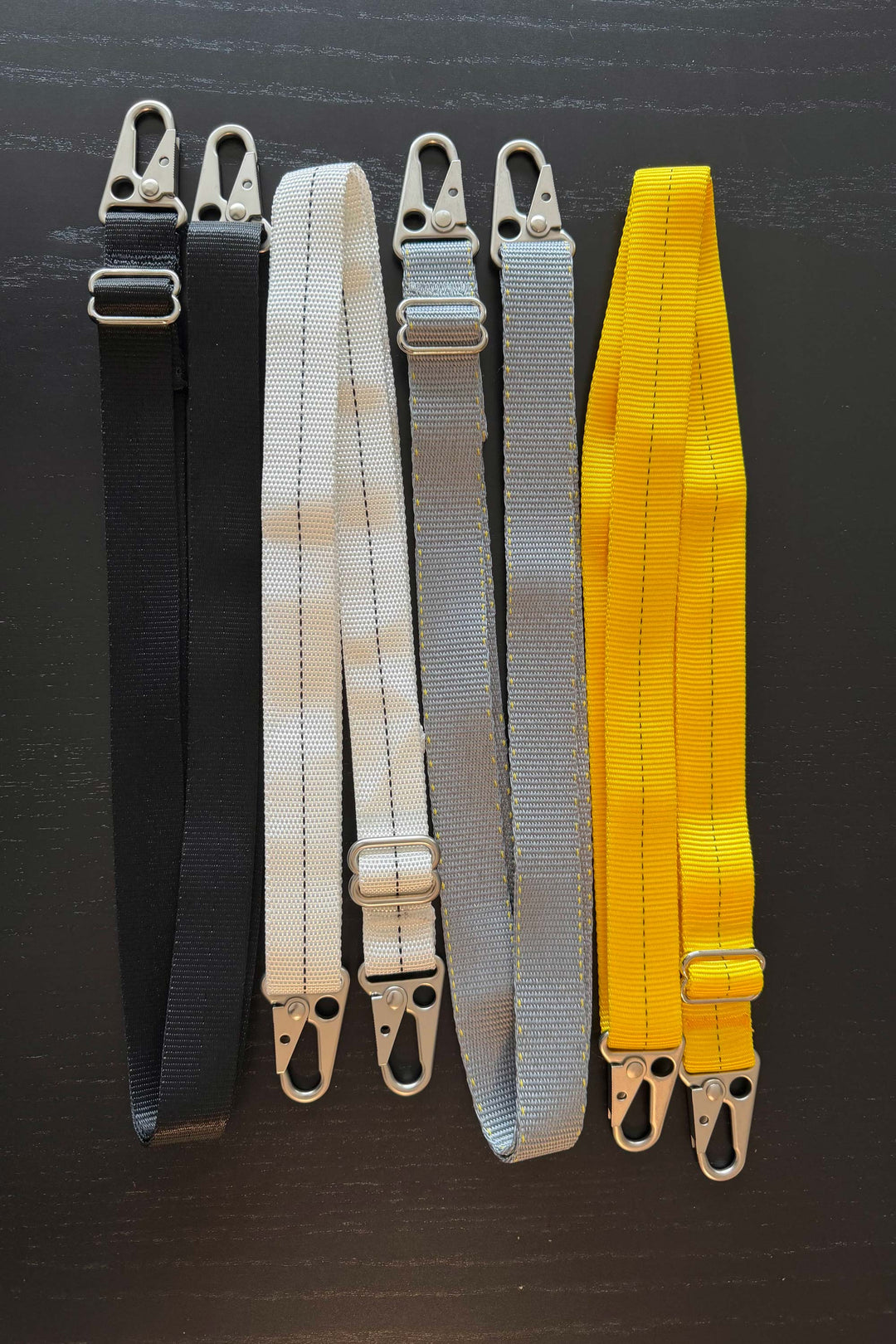 Four straps in black, white, gray, and yellow with metal clasps on a dark background